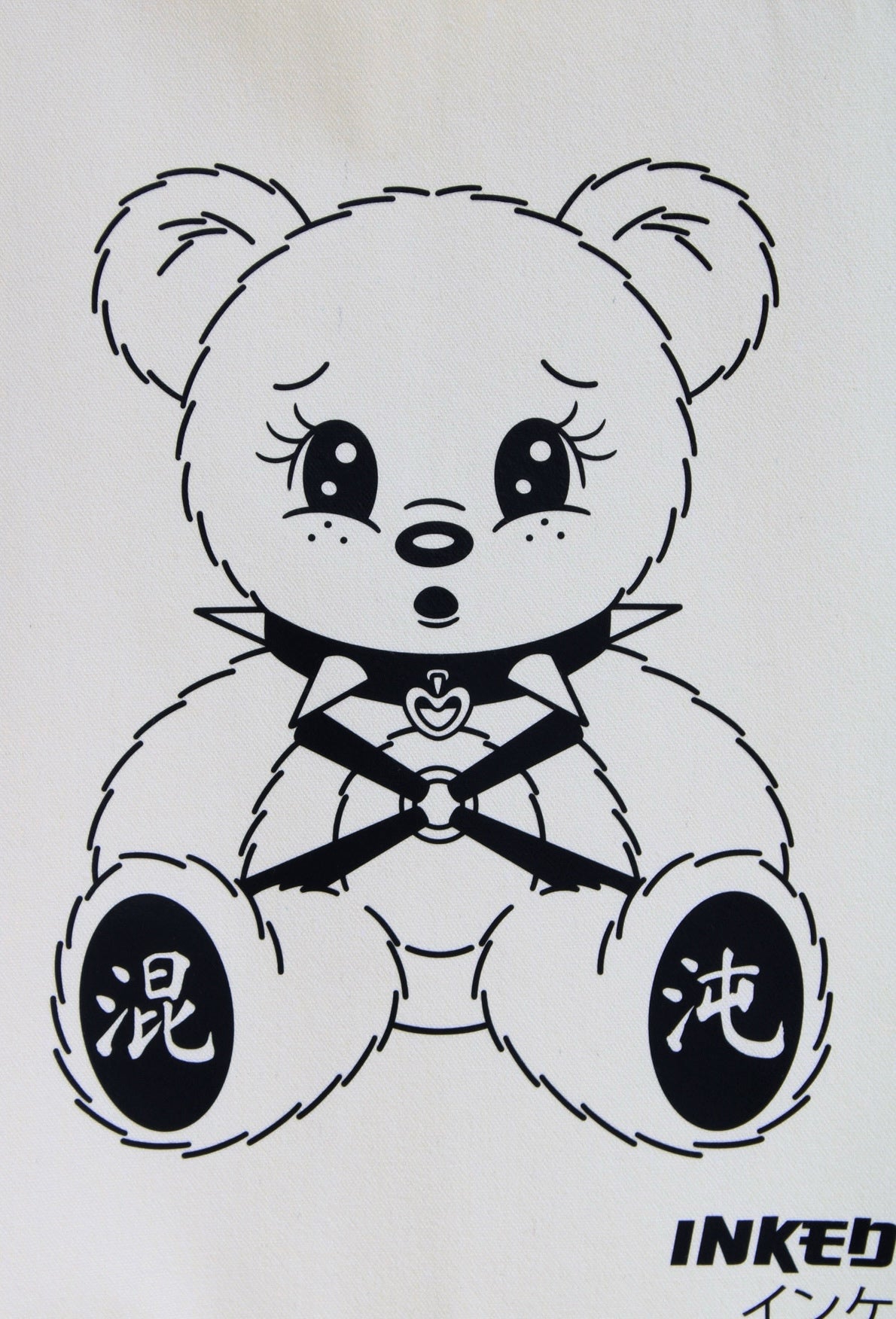 Black and white line art illustration of a cute teddy bear with large eyes, a bow tie, and Japanese characters on its feet, on a white background.